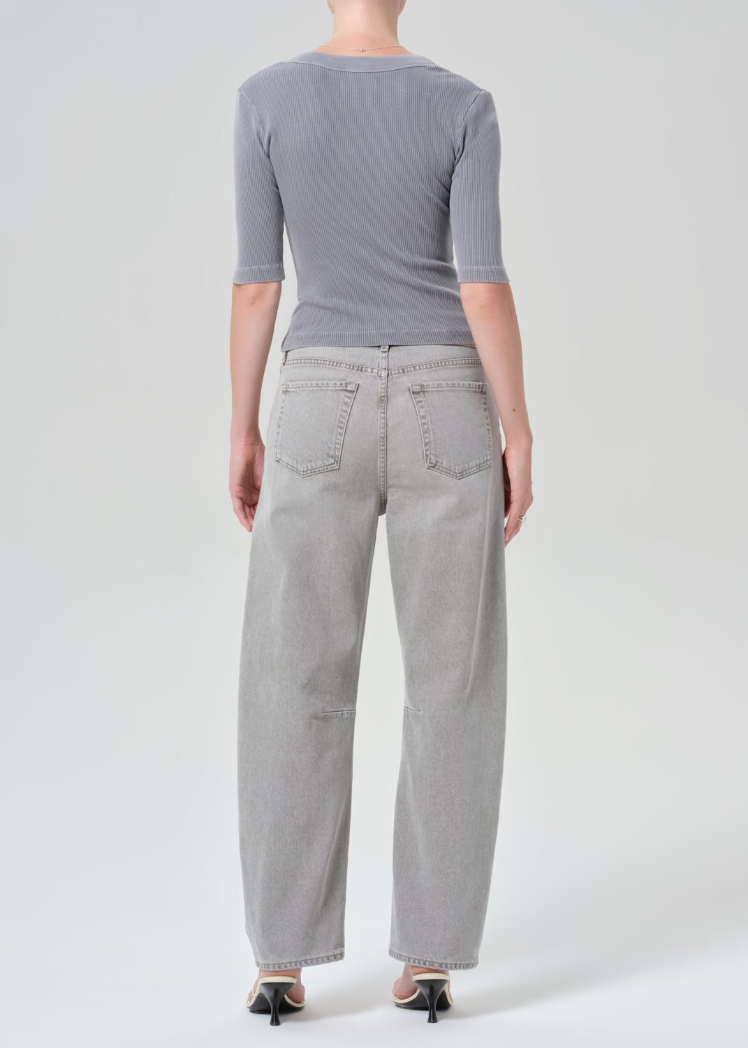 Person wearing a gray top and light gray pants on a white background