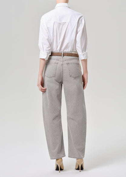 A model shown from the back wearing light grey wide-leg jeans, a white button-down shirt, a brown belt, and beige heels against a grey background.