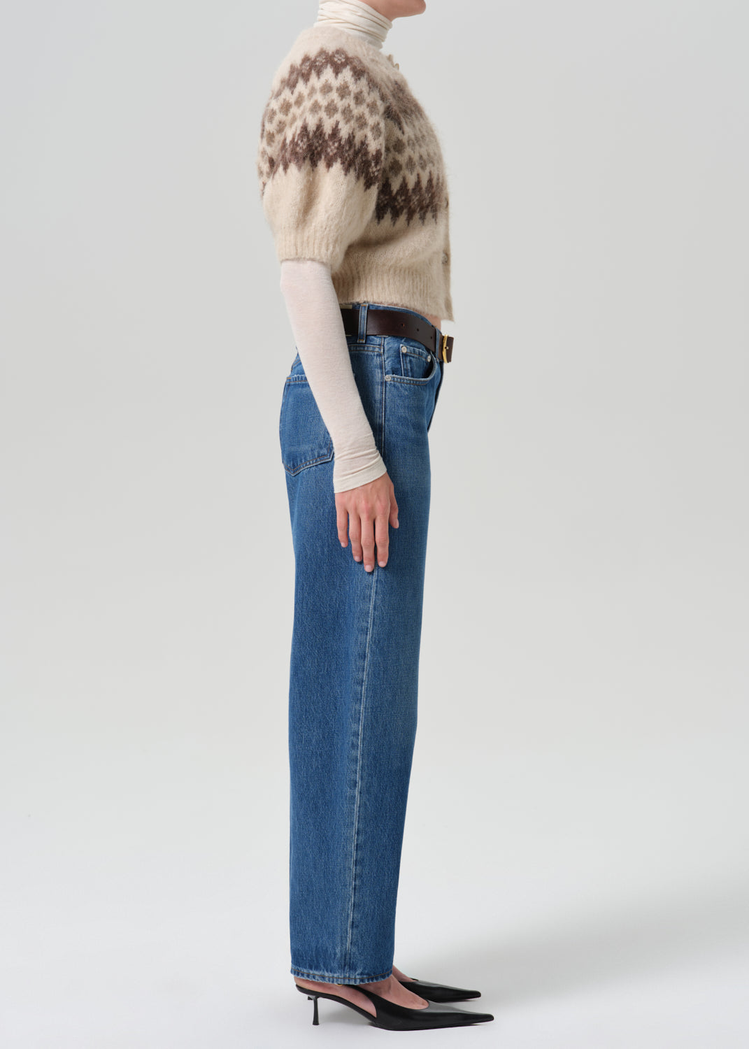 Person wearing a printed sweater with blue pants on a grey background