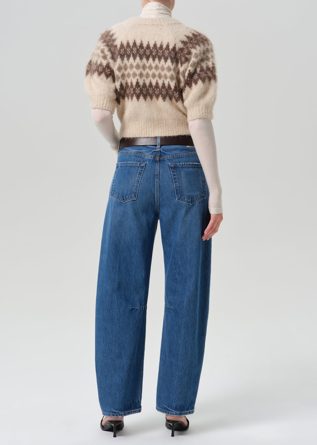 Person wearing a printed sweater with blue pants on a grey background