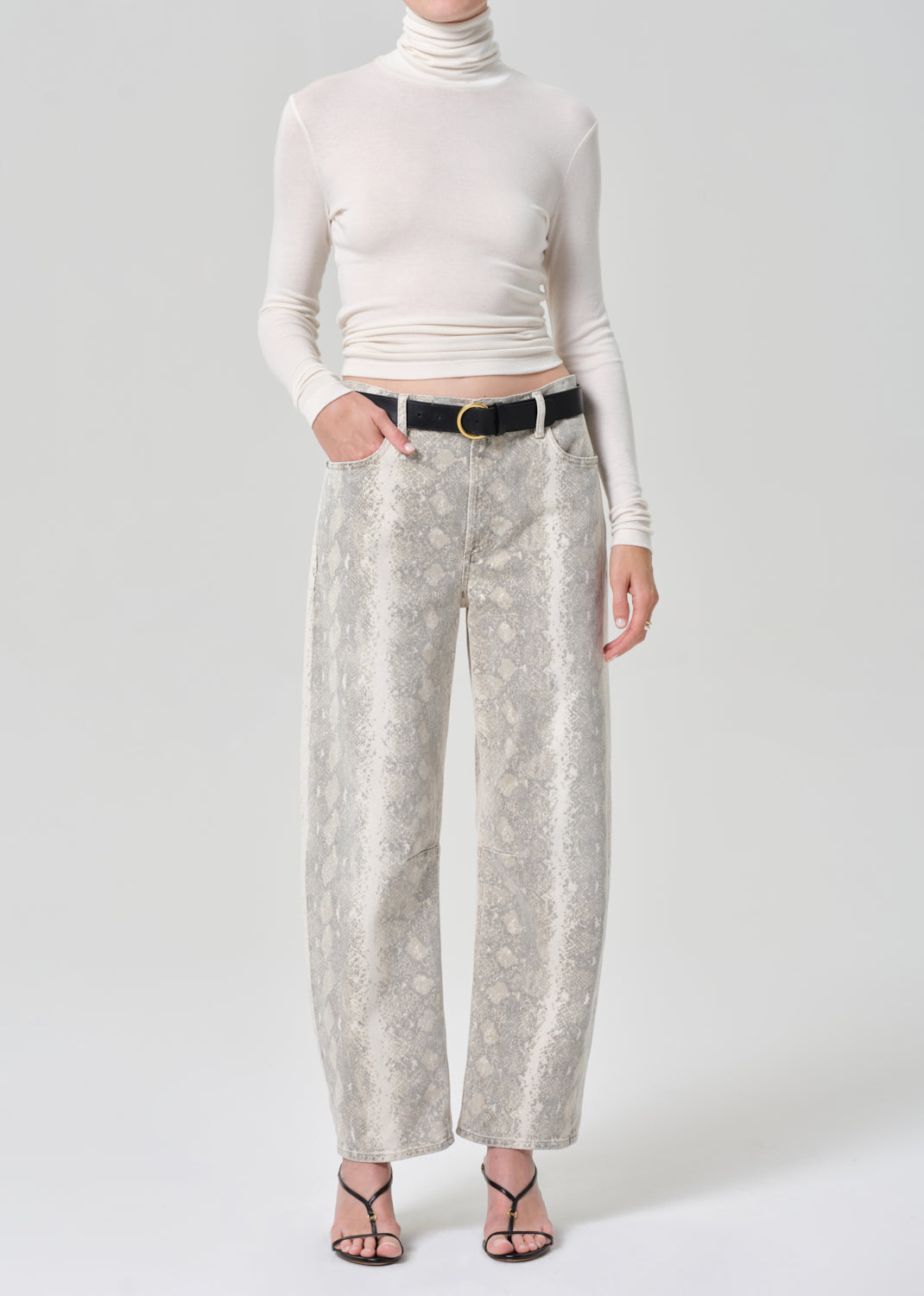 Person wearing a white turtleneck and python patterned jeans on a grey background