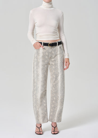 Person wearing a white turtleneck and python patterned jeans on a grey background