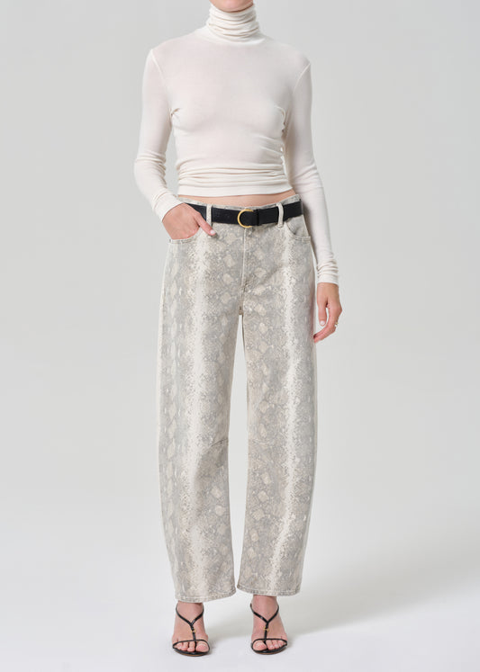 Person wearing a white turtleneck and python patterned jeans on a grey background
