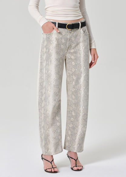 Person wearing a white turtleneck and python patterned jeans on a grey background