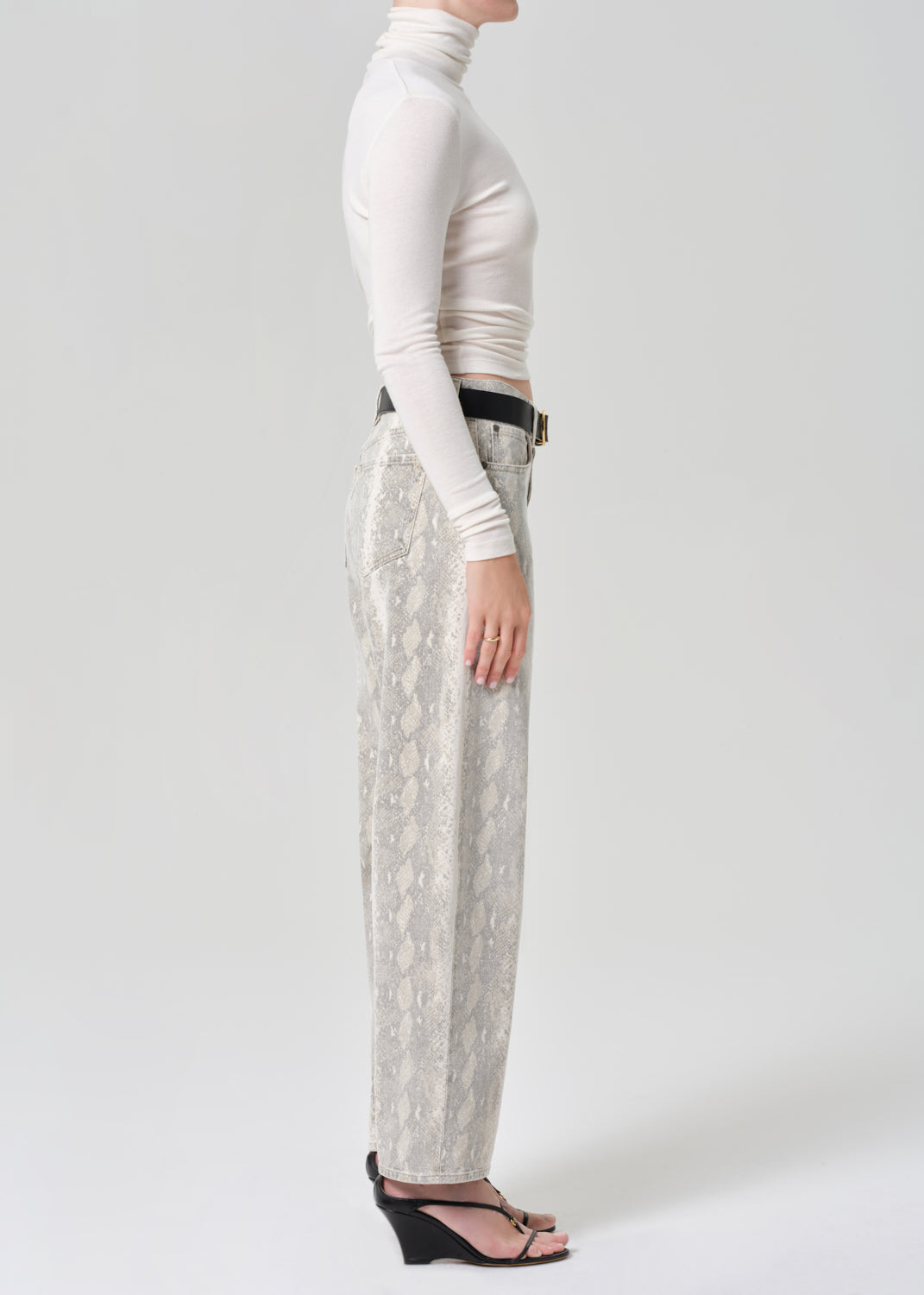 Person wearing a white turtleneck and python patterned jeans on a grey background