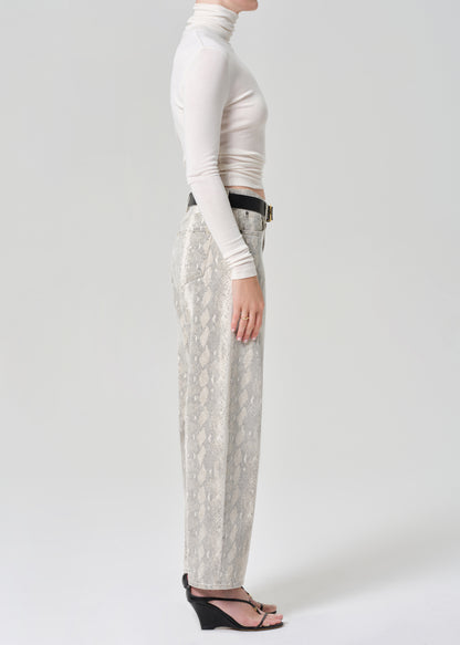 Person wearing a white turtleneck and python patterned jeans on a grey background
