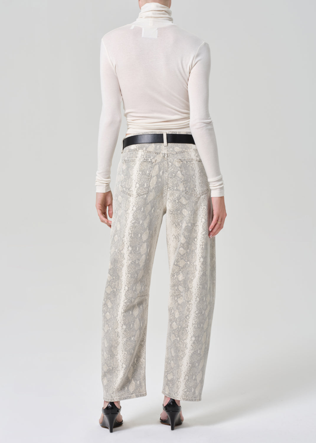 Person wearing a white turtleneck and python patterned jeans on a grey background