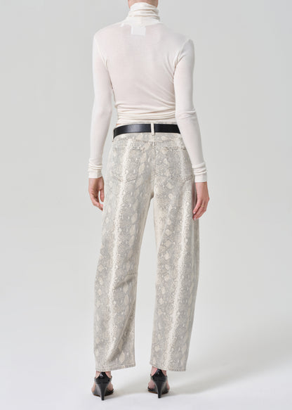 Person wearing a white turtleneck and python patterned jeans on a grey background