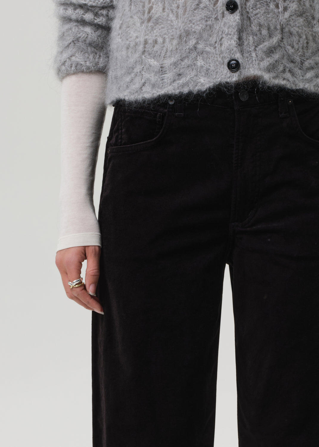 Person wearing a gray sweater and black velvet pants on a grey background