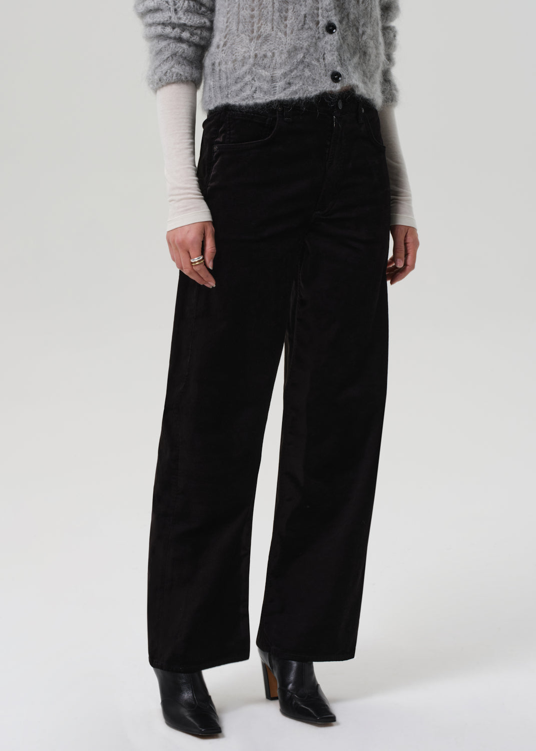 Person wearing a gray sweater and black velvet pants on a grey background