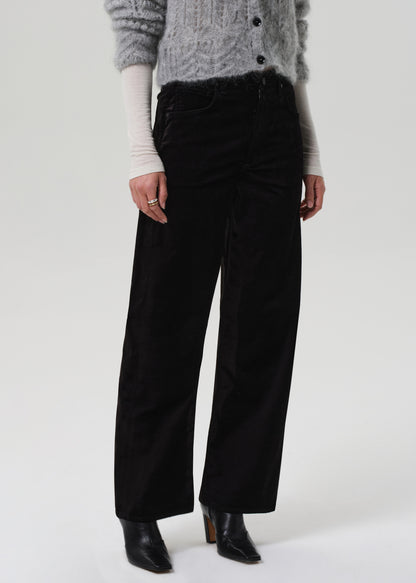 Person wearing a gray sweater and black velvet pants on a grey background