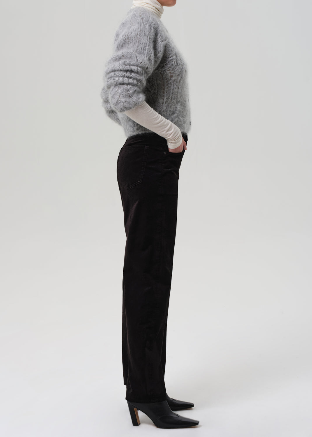 Person wearing a gray sweater and black velvet pants on a grey background
