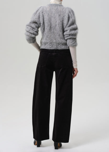 Person wearing a gray sweater and black velvet pants on a grey background