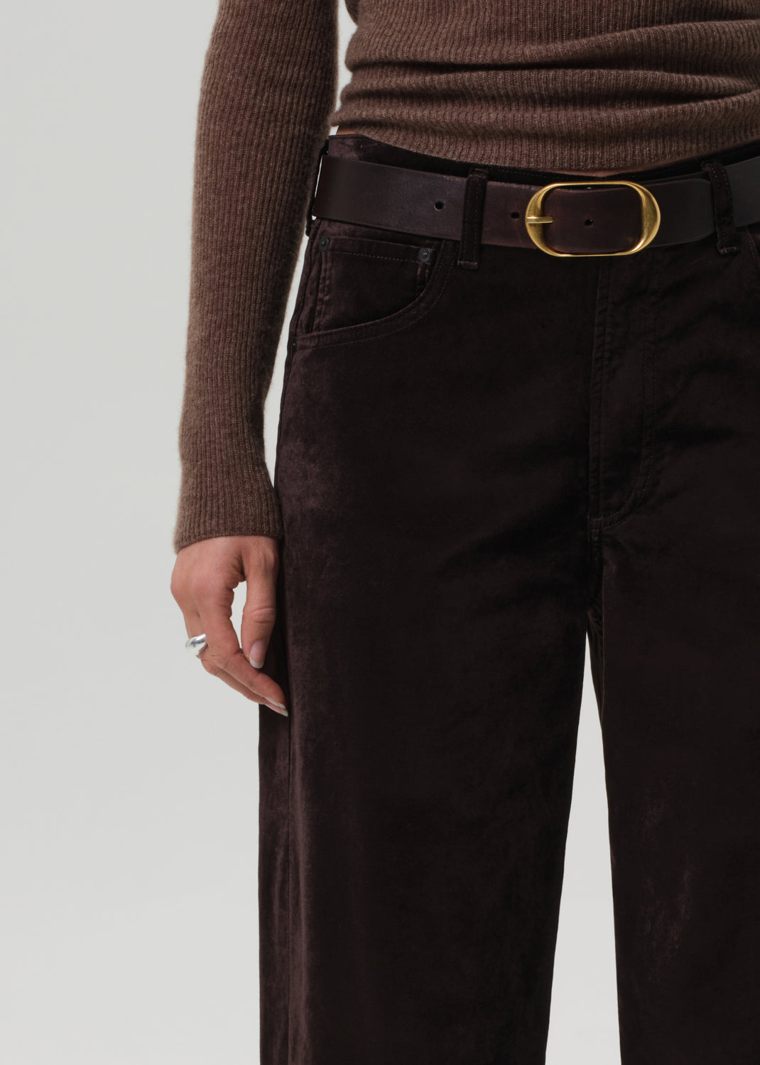 Person wearing a brown sweater and dark brown velvet pants on a grey background