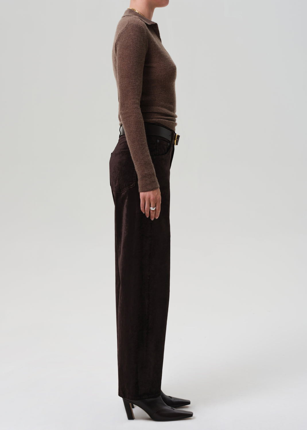 Person wearing a brown sweater and dark brown velvet pants on a grey background