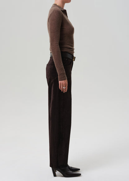 Person wearing a brown sweater and dark brown velvet pants on a grey background