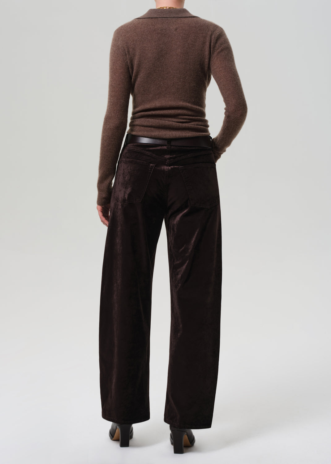 Person wearing a brown sweater and dark brown velvet pants on a grey background