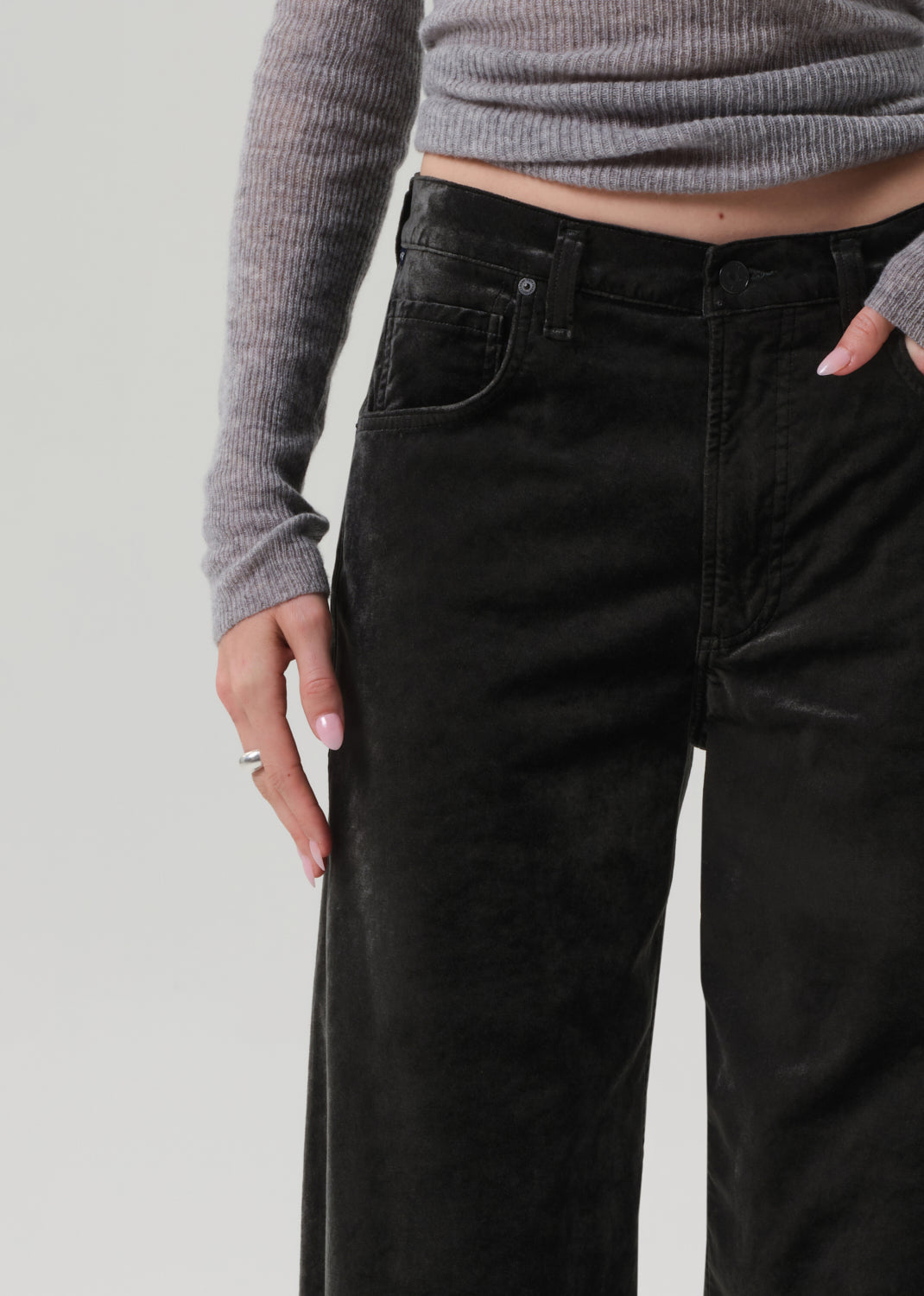 Person wearing a gray sweater and green wide-leg velvet pants on a grey background