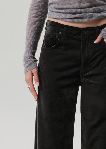 Person wearing a gray sweater and green wide-leg velvet pants on a grey background