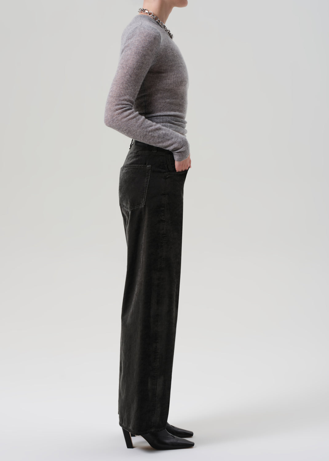 Person wearing a gray sweater and green wide-leg velvet pants on a grey background