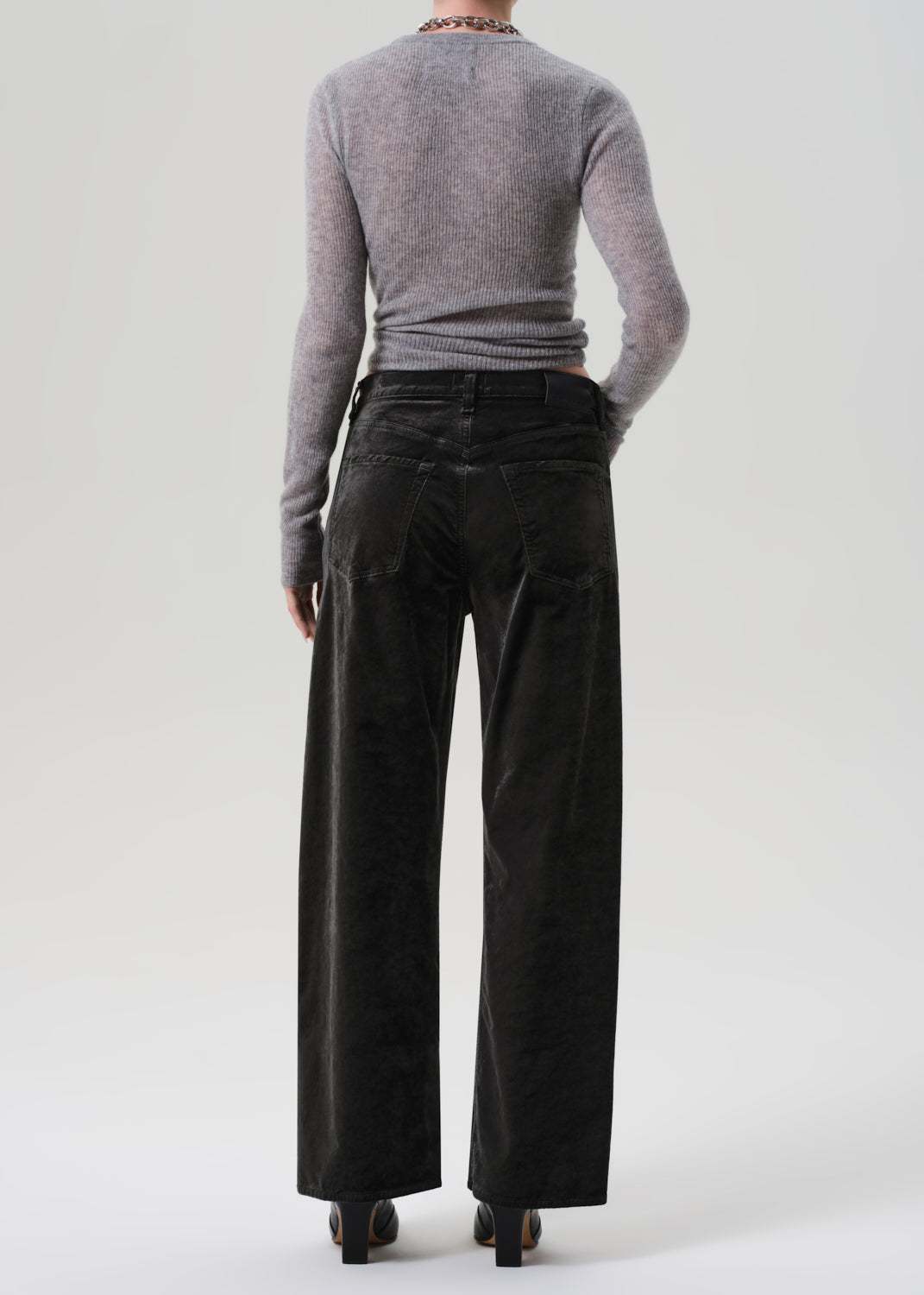 Person wearing a gray sweater and green wide-leg velvet pants on a grey background