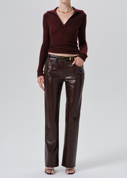 A model wearing a dark burgundy ribbed knit polo-neck long-sleeve top and matching dark brown faux-leather wide-leg trousers, styled with a black belt and metallic buckle, against a grey background.