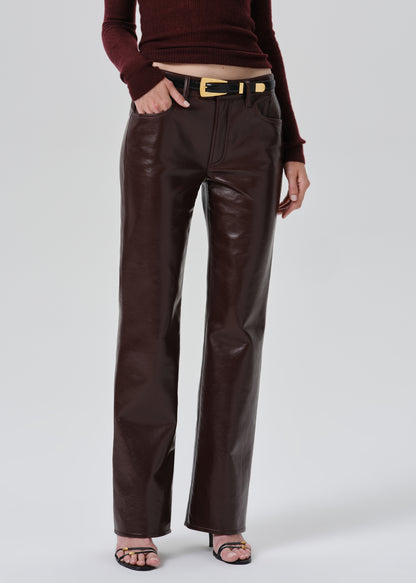 A model wearing dark brown faux-leather wide-leg pants with a black belt featuring a gold buckle, styled with a burgundy ribbed knit top and black sandals against a grey background.