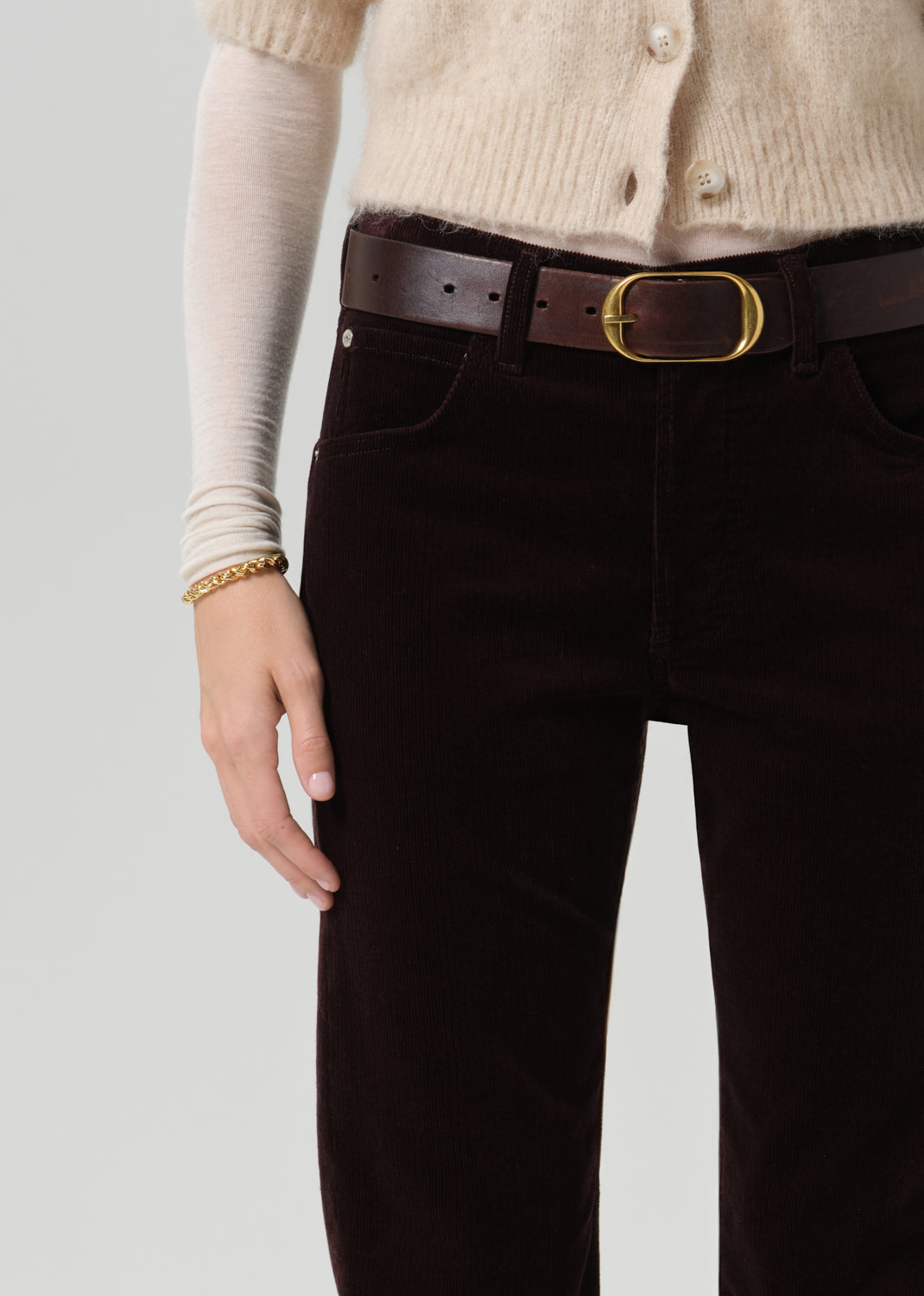 Person wearing dark brown straight leg jeans on a grey background