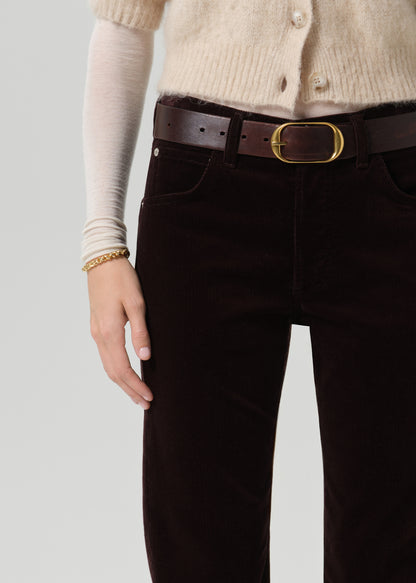 Person wearing dark brown straight leg jeans on a grey background