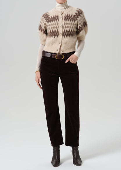 Person wearing dark brown straight leg jeans with a cream patterned short sleeve sweater on a grey background