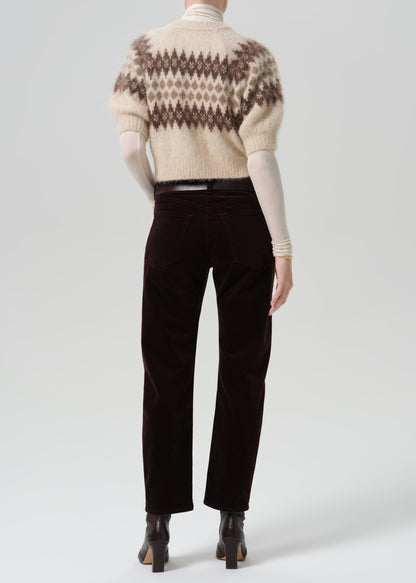 Person wearing dark brown straight leg jeans with a cream patterned short sleeve sweater viewed from the back on a grey background