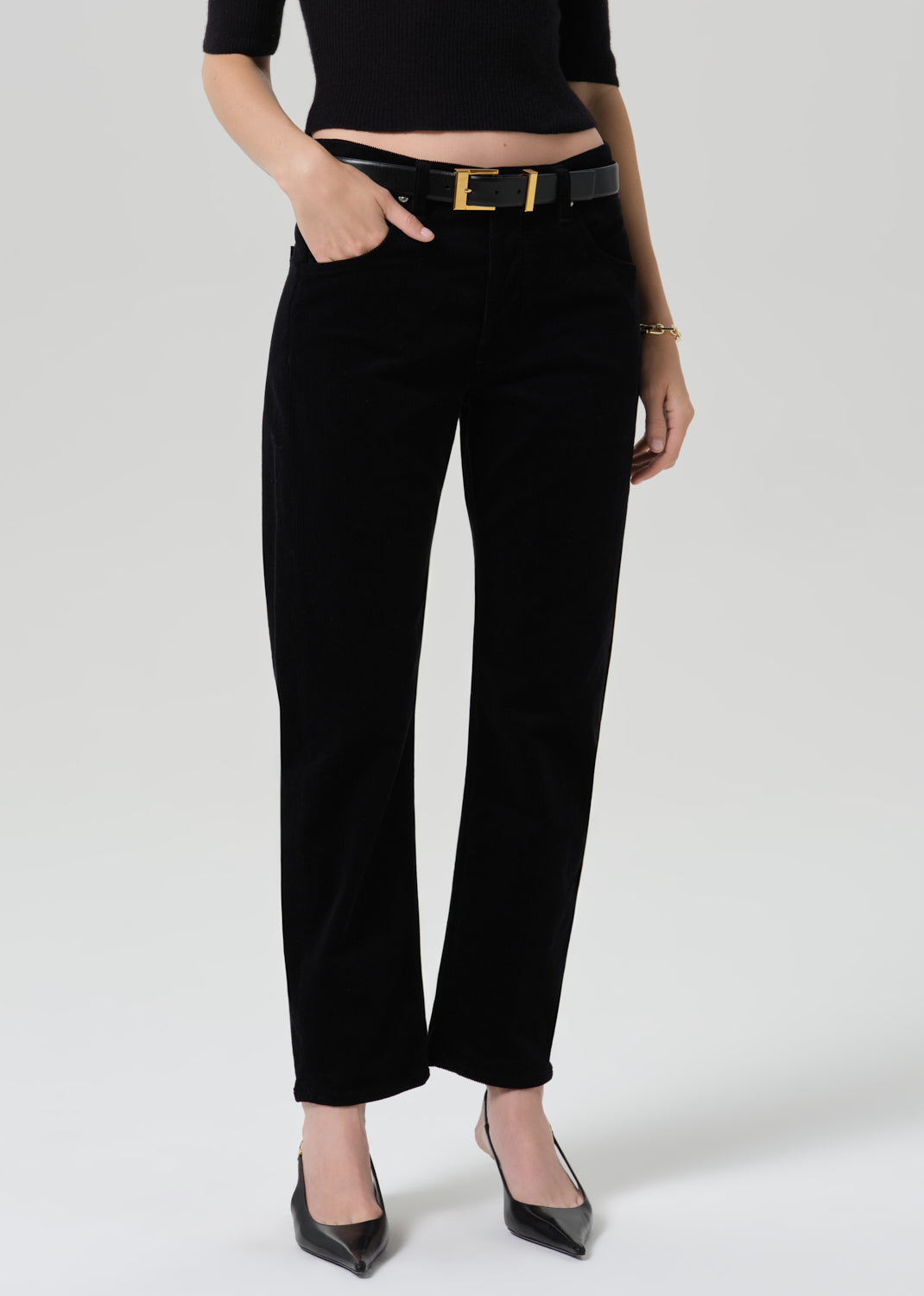 Person wearing black straight leg jeans with a black short sleeve top and black pointed toe heels on a grey background
