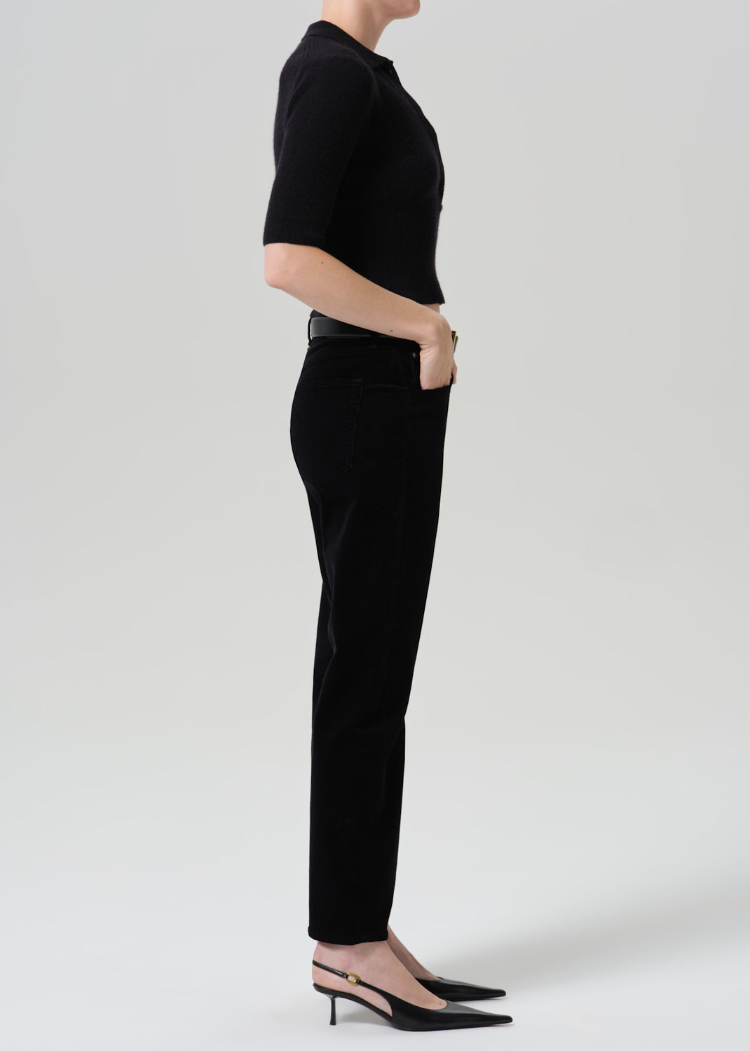 Person wearing black straight leg jeans with a black short sleeve top viewed from the side on a grey background