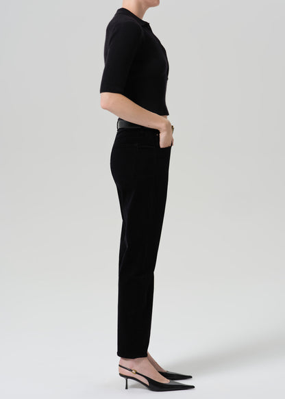 Person wearing black straight leg jeans with a black short sleeve top viewed from the side on a grey background