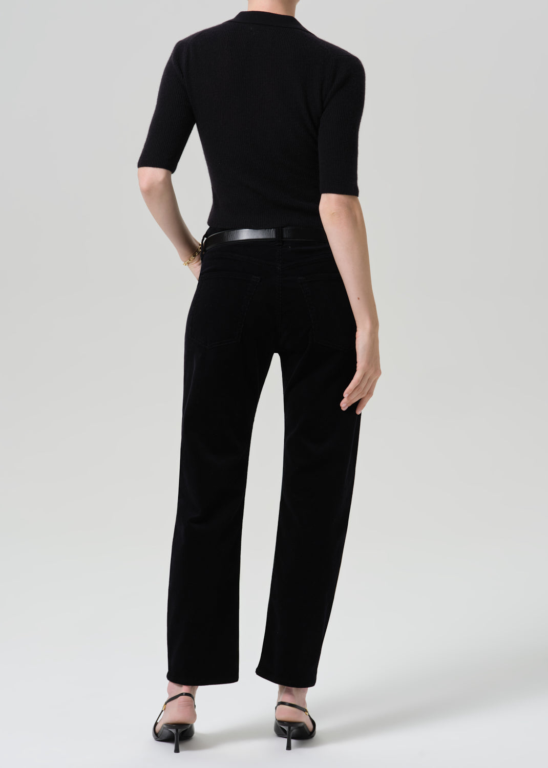 Person wearing black straight leg jeans with a black short sleeve top viewed from the back on a grey background