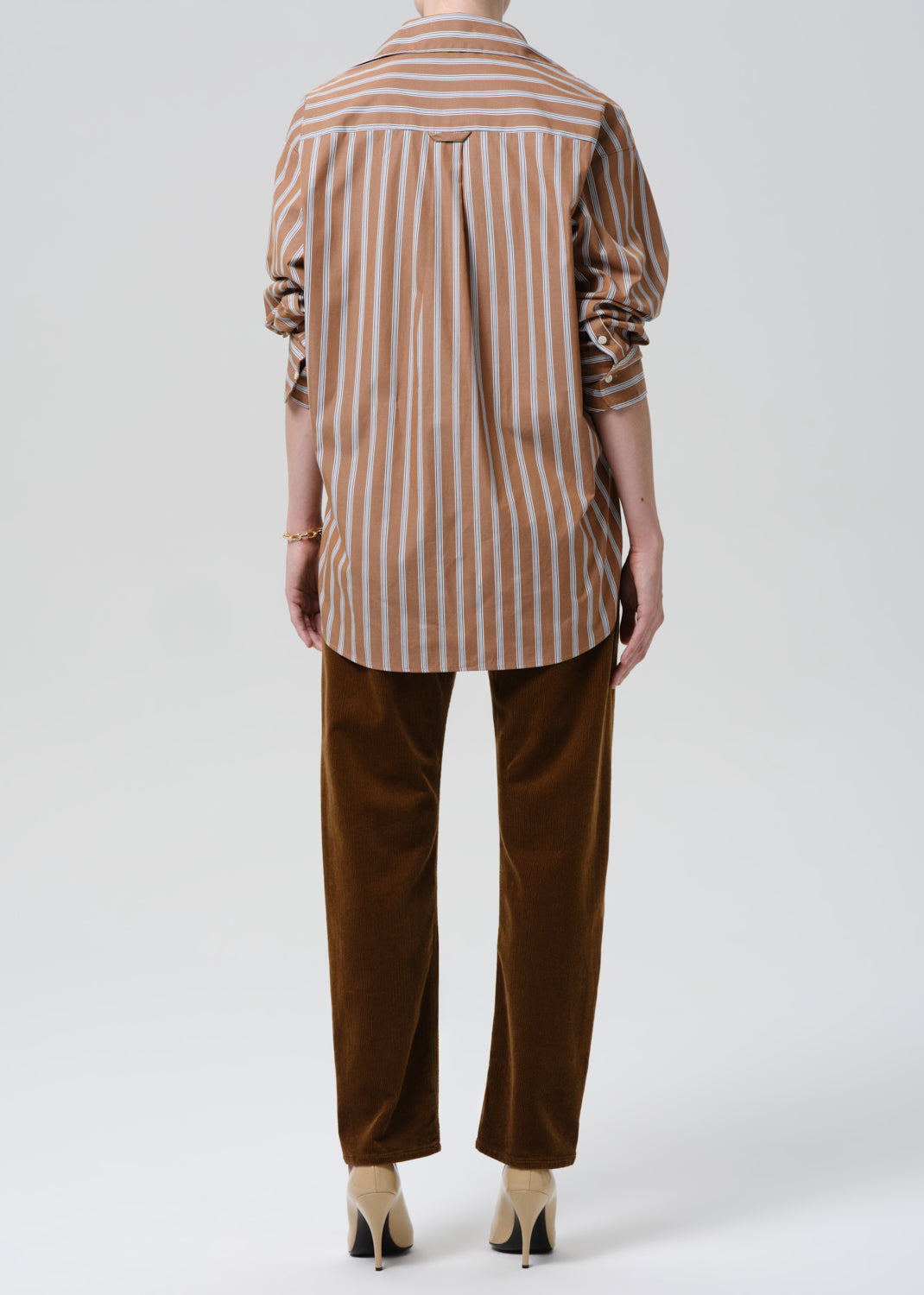Person wearing a brown and white striped shirt with brown pants on a grey background