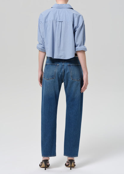 Person wearing a blue shirt and jeans on a plain background