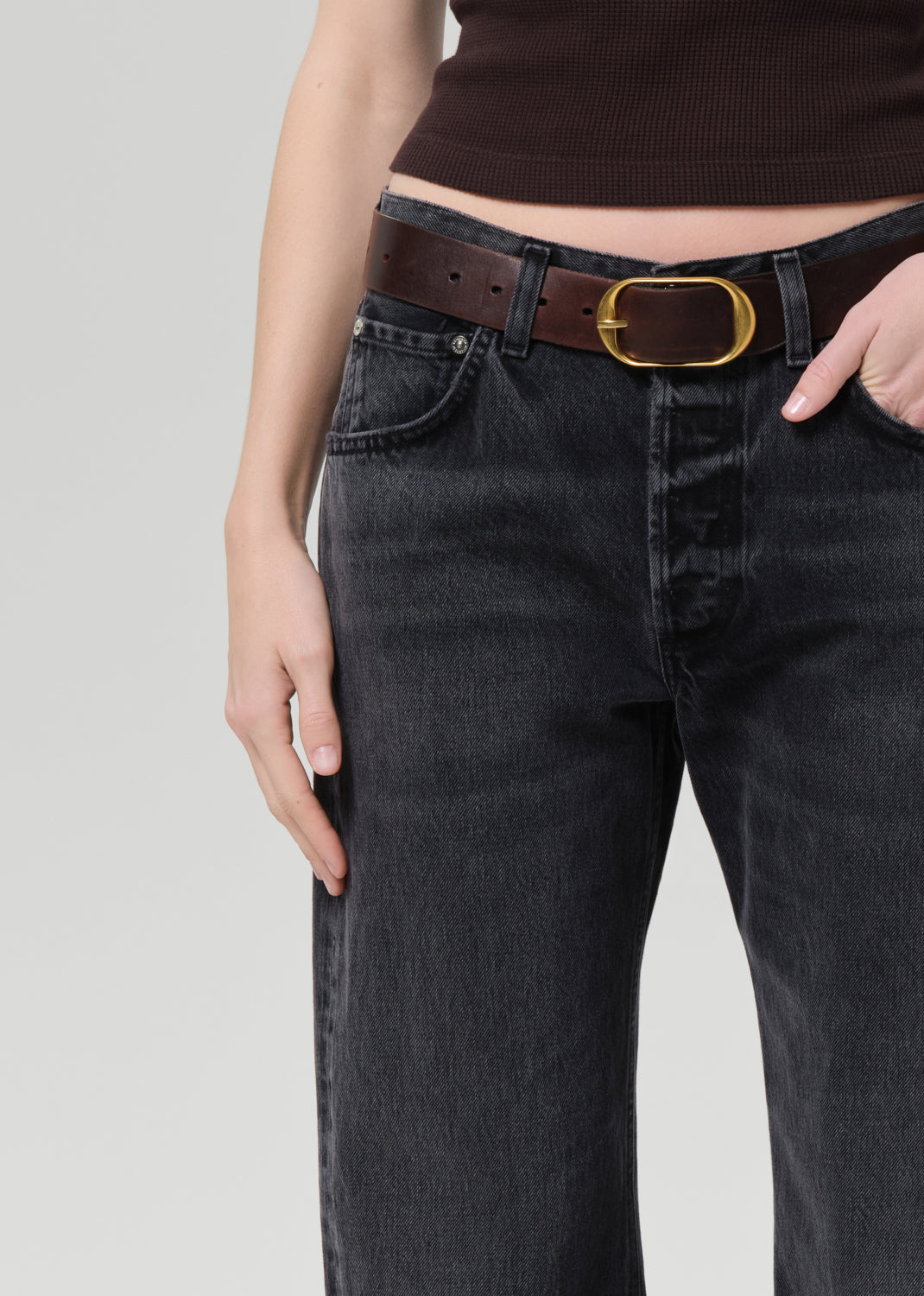 Person wearing black jeans with a brown belt on a light gray background