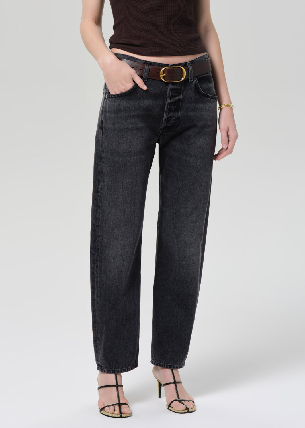 Person wearing black jeans with a gold belt on a plain background