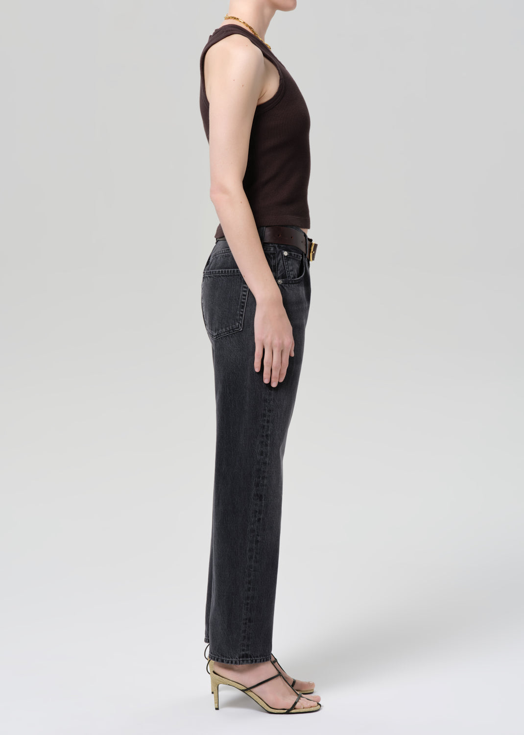 Person wearing black high-waisted jeans and a brown sleeveless top on a light gray background