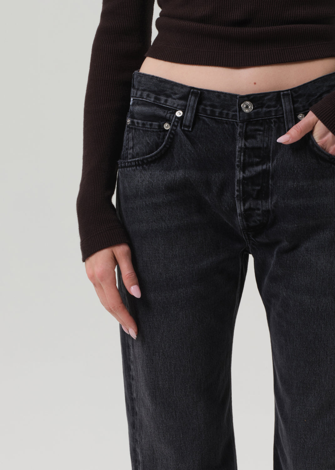 Person wearing black jeans and a brown top on a grey background