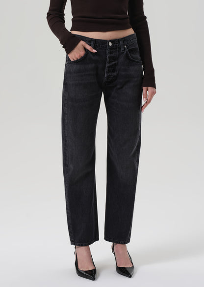 Person wearing black jeans and a brown top on a grey background