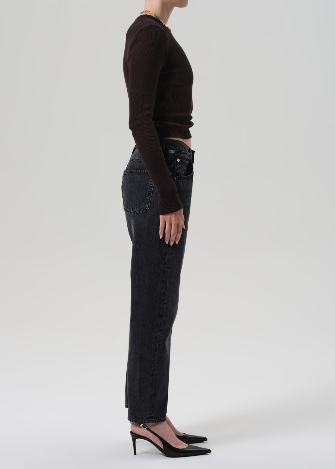 Person wearing black jeans and a brown top on a grey background