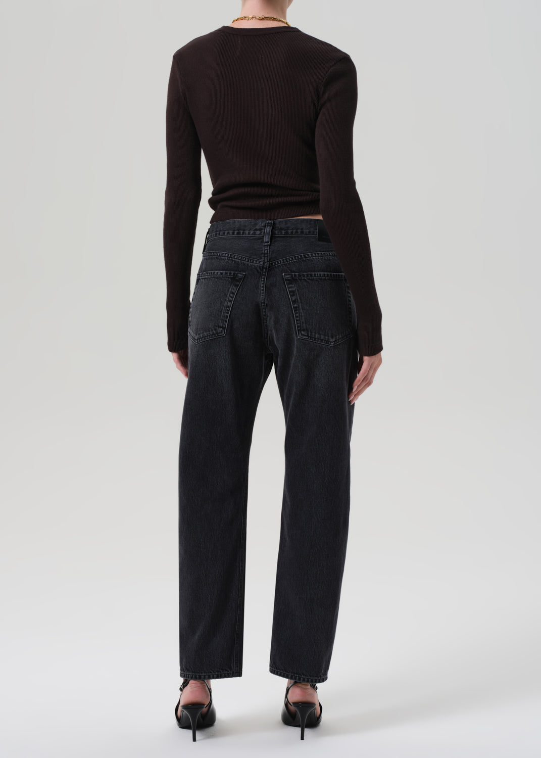 Person wearing black jeans and a brown top on a grey background