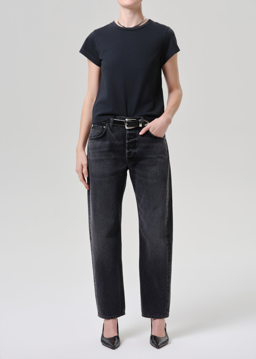 Person wearing a black t-shirt and black jeans on a grey background.