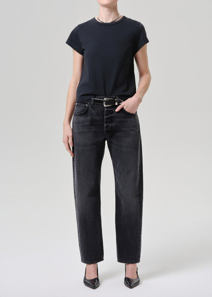 Person wearing a black t-shirt and black jeans on a grey background.