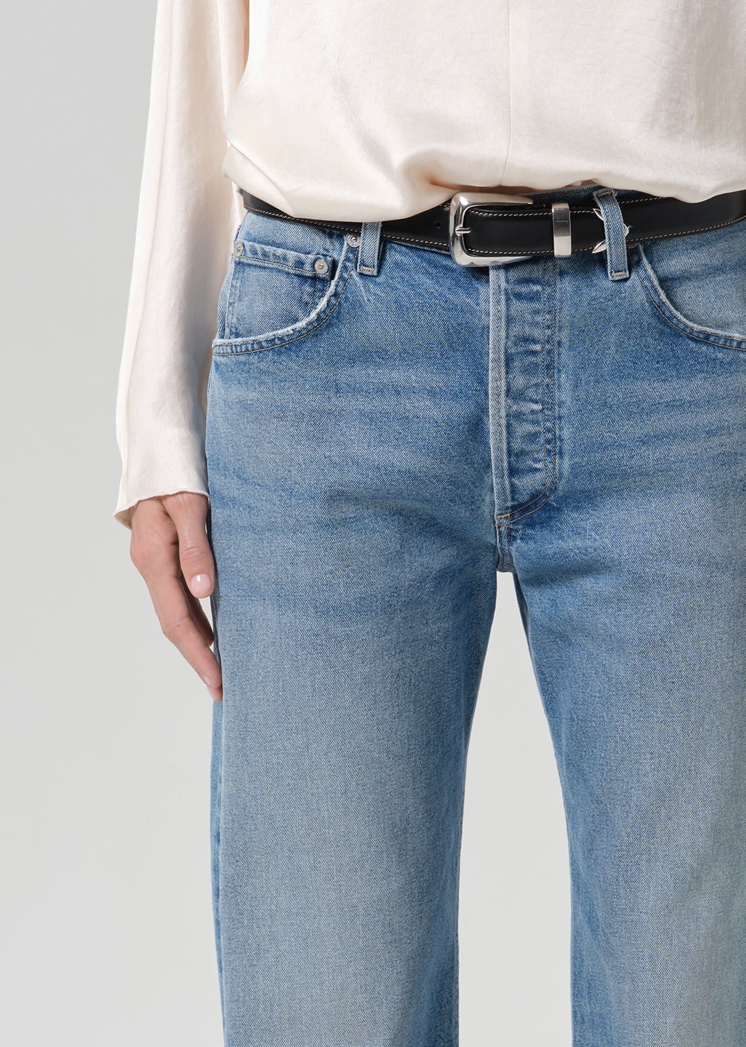 Person wearing blue jeans with cream color satin top