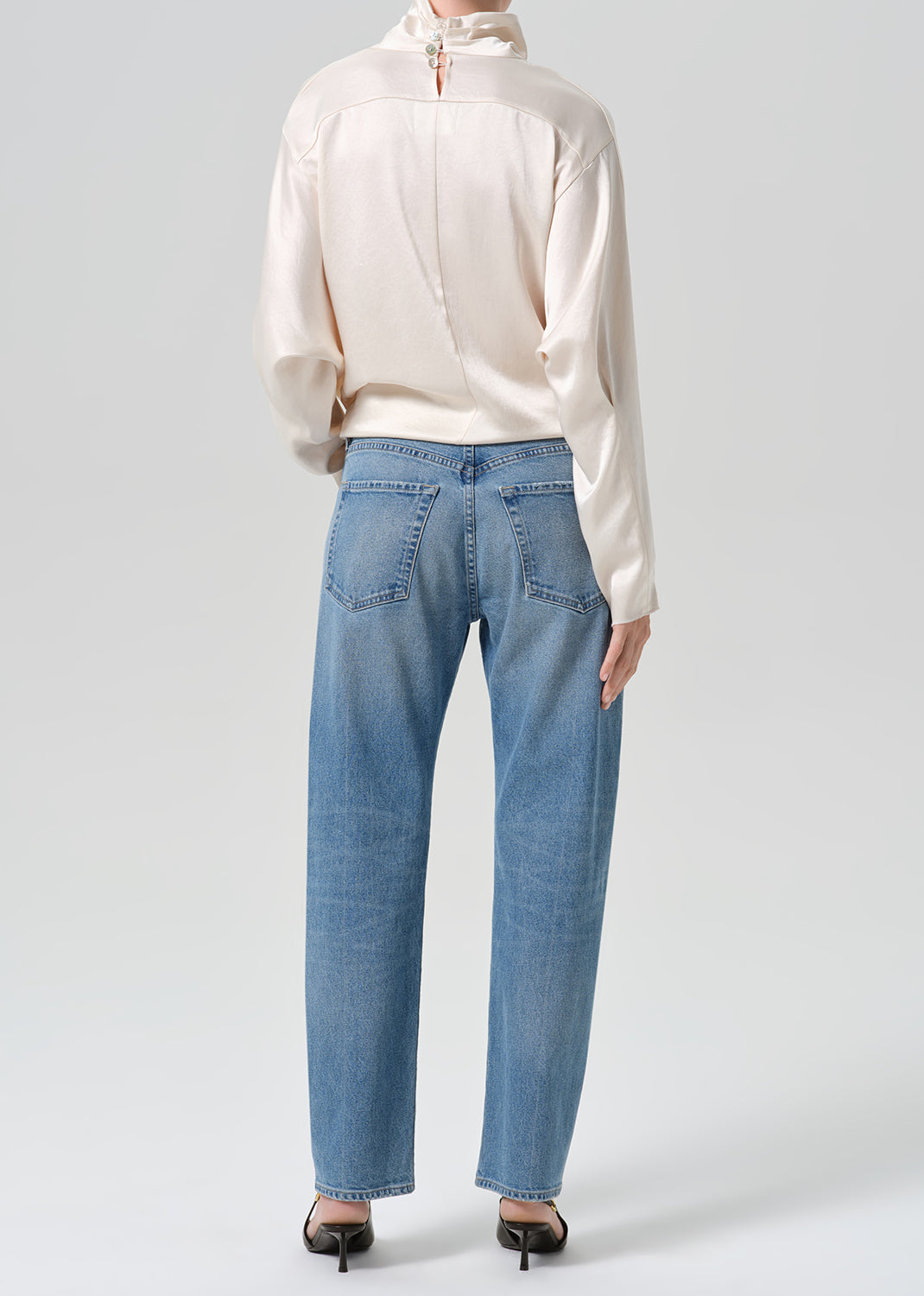 Person wearing blue jeans with cream color satin top