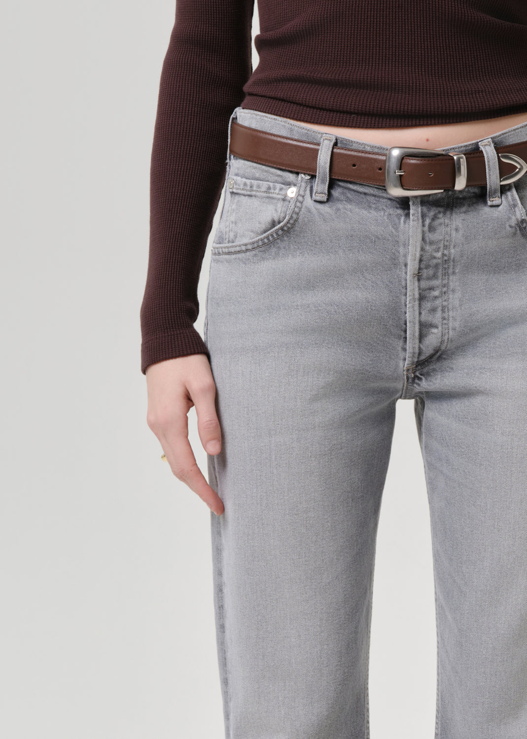Person wearing gray jeans with a brown belt on a grey background