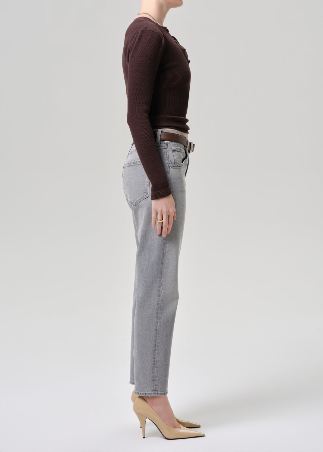 Person wearing a brown long-sleeve top and gray jeans on a grey background